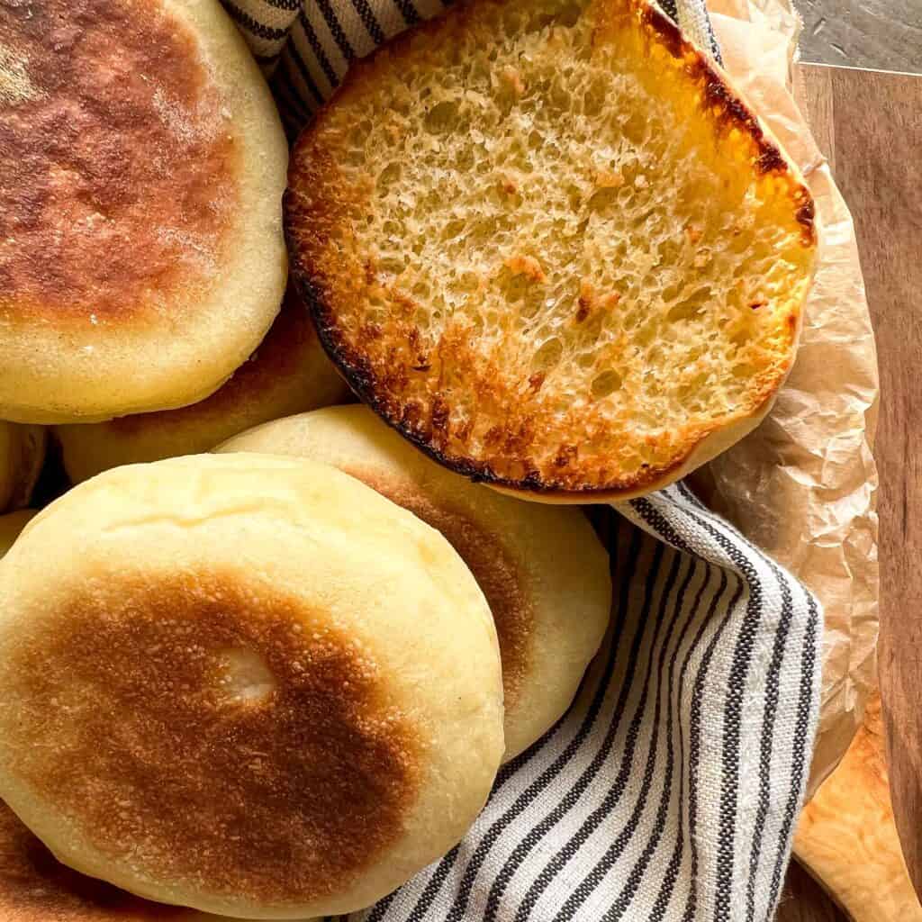 A close up view of english muffins showing a large crumb and half of a toasted muffin.
